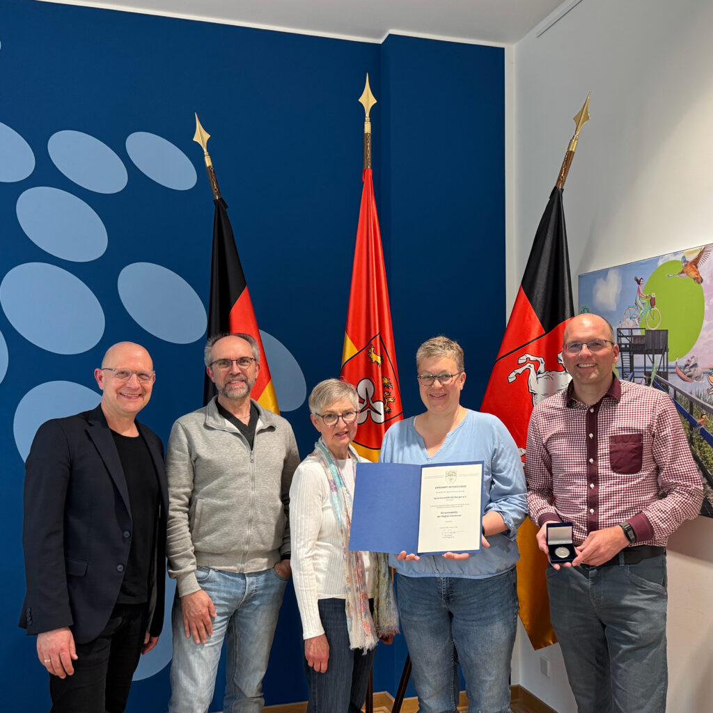 Foto von fünf Personen, die eine Medaille und eine Urkunde präsentieren.