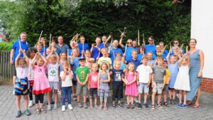 Gruppenfoto Musikverein, vorne Kinder, hinten Erwachsene in blauen Hemden, teils die Arme fröhlich erhoben.